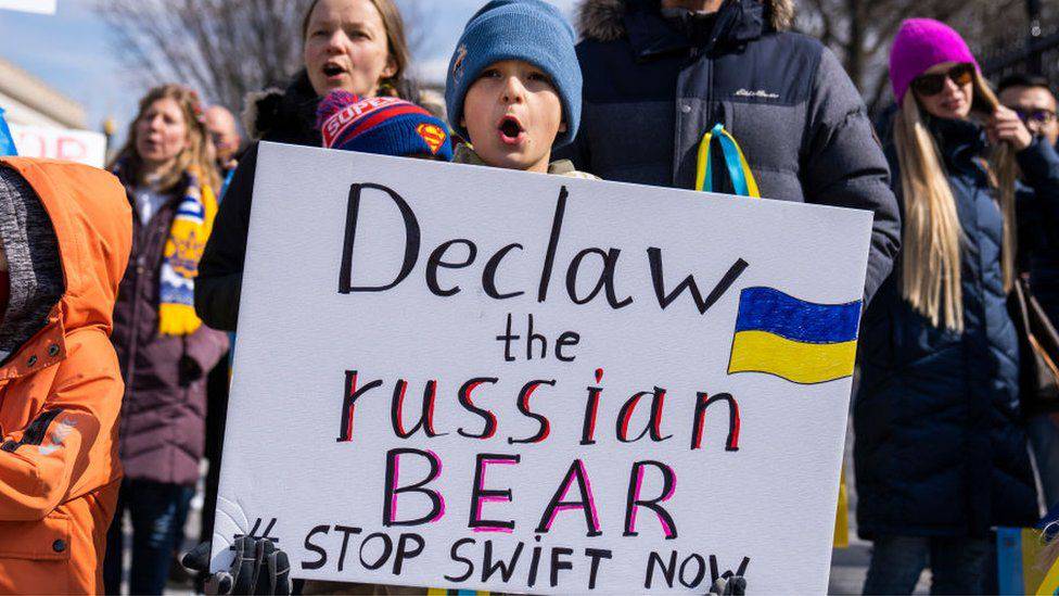Un niño ucraniano sosteniendo una pancarta que lee: "Sáquenle las garras al oso ruso, detengan el SWIFT ahora". Foto: AFP.