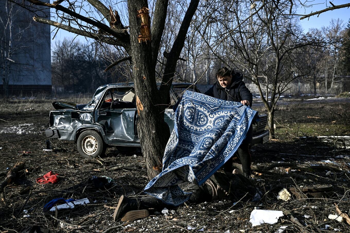 EDITORS NOTE: Graphic content / A man uses a carpet to cover a body stretched out on the ground after bombings on the eastern Ukraine town of Chuguiv on February 24, 2022, as Russian armed forces are trying to invade Ukraine from several directions, using rocket systems and helicopters to attack Ukrainian position in the south, the border guard service said. - Russia's ground forces on Thursday crossed into Ukraine from several directions, Ukraine's border guard service said, hours after President Vladimir Putin announced the launch of a major offensive. Russian tanks and other heavy equipment crossed the frontier in several northern regions, as well as from the Kremlin-annexed peninsula of Crimea in the south, the agency said. (Photo by Aris Messinis / AFP)
