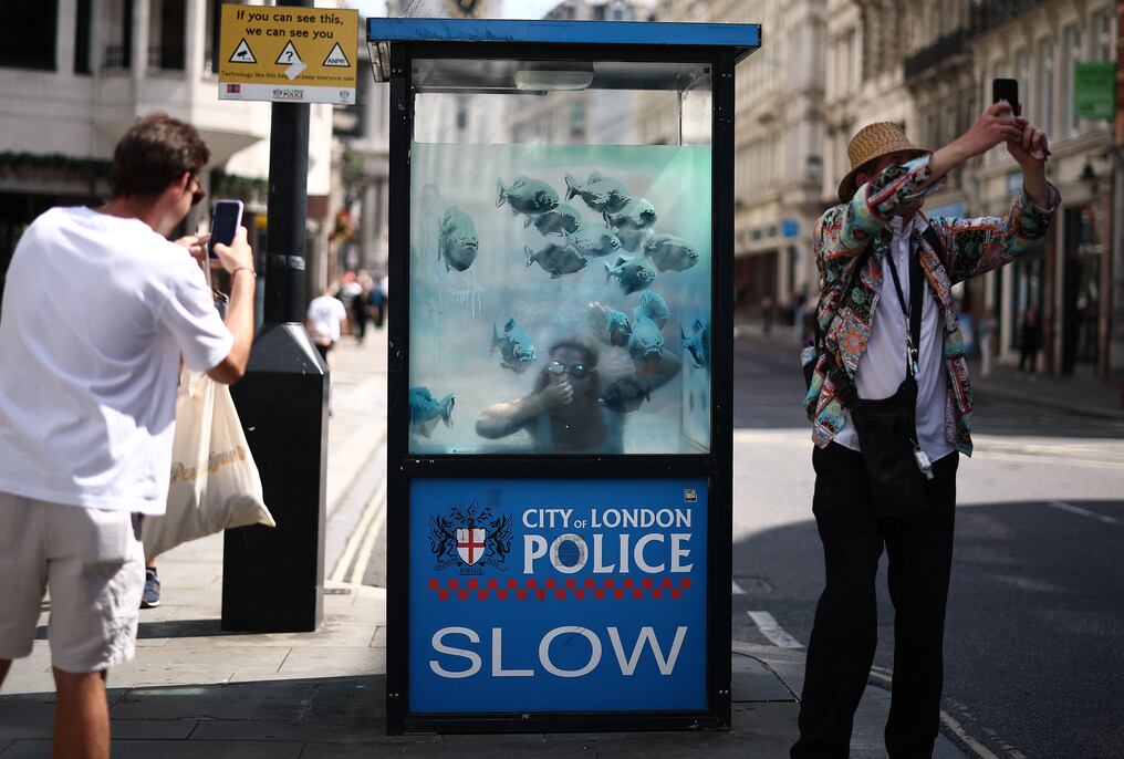 Una persona posa con la séptima obra de arte lanzada esta semana, que muestra peces nadando alrededor de una cabina de policía. Foto: AFP