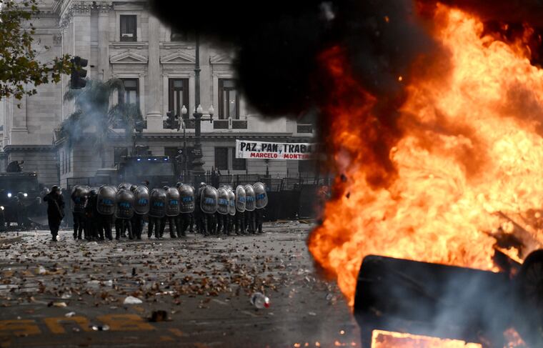 Anti-riot police officers stand guard behind a Cadena 3 radio station car on fire during a protest outside the National Congress in Buenos Aires on June 12, 2024. Argentine senators are discussing a key reform package for the ultra-right-wing president Javier Milei, in a session marked by strikes and demonstrations in front of Congress. (Photo by Luis ROBAYO / AFP)
