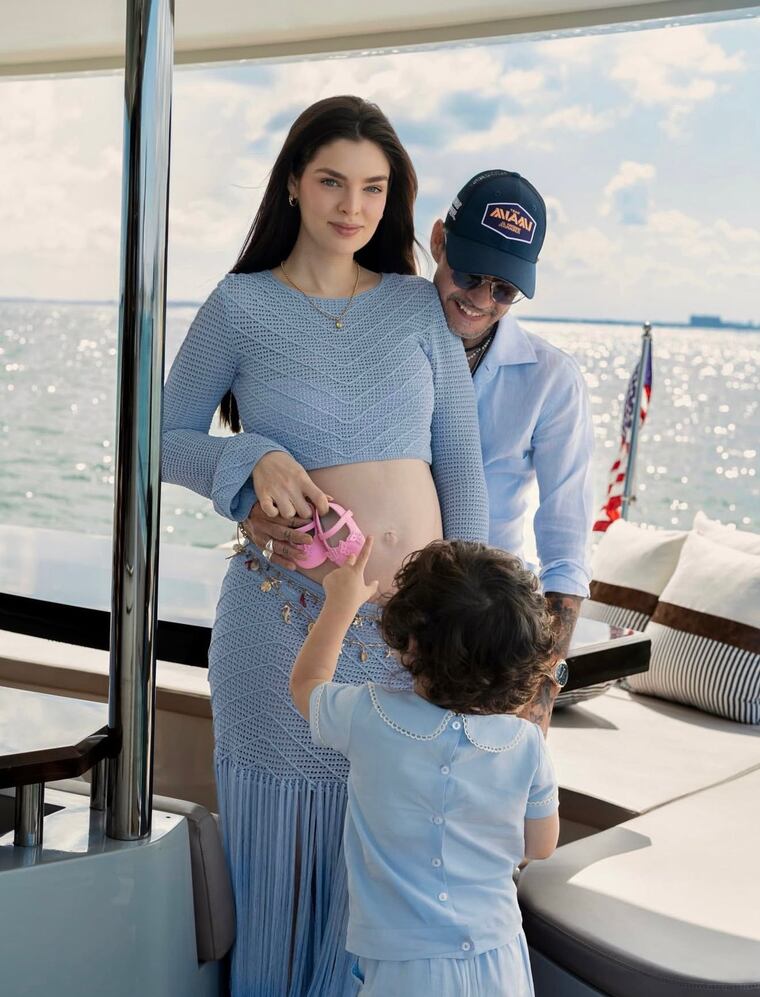 Nadia Ferreira, Marc Anthony y su hijo Marco, posan con unos diminutos zapatos en color rosa, indicando el nacimiento de una niña.