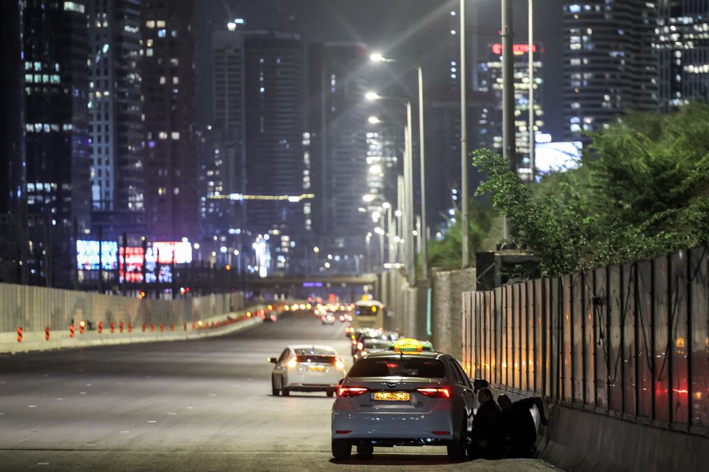 La gente se refugia detrás de un vehículo estacionado al costado de una carretera en Tel Aviv al sonar las sirenas de ataque aéreo. Foto: AFP