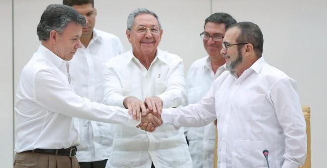 El presidente Juan Manuel Santos se da la mano con el jefe de las FARC, Rodrigo Londoño Timochenko. El presidente de Cuba, Raúl Castro, sonríe.