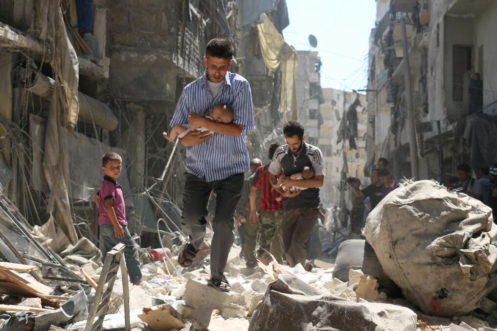 Hombres sirios cargan a bebés en medio de las ruinas de una de las zonas más afectadas de Alepo. Foto: AMEER ALHALBI / AFP