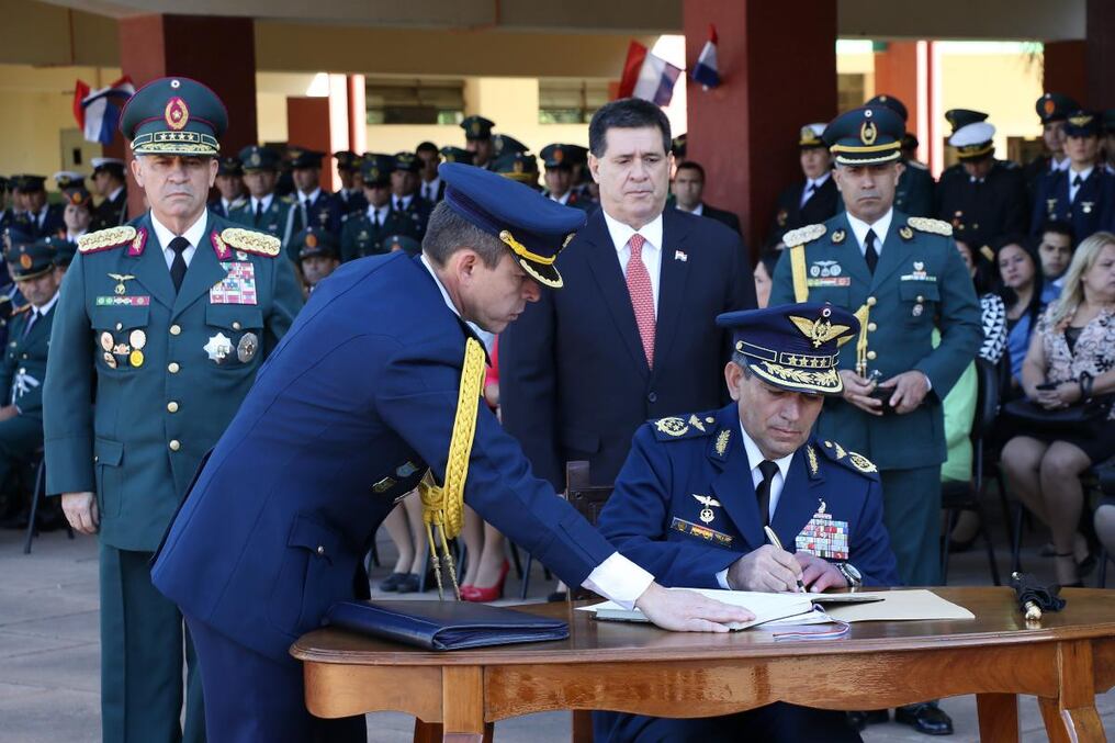 Piris firma el acta. Atrás observan el Presidente y Garcete. 