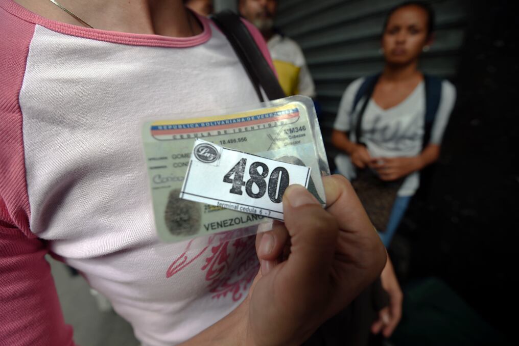 Una mujer muestra el número de espera que le corresponde para comprar comida a las afuera de un supermercado en Caracas, Venezuela. Foto: AFP / JUAN BARRETO.