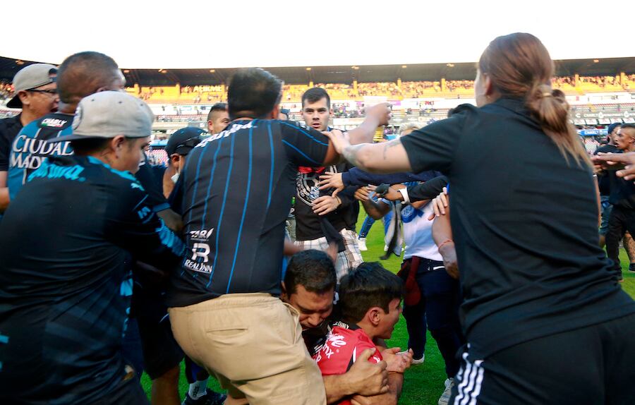 La violencia de las gradas se trasladó al césped del estadio. En la foto, un padre protege a su hijo menor
en medio de la pelea.FOTO:AFP