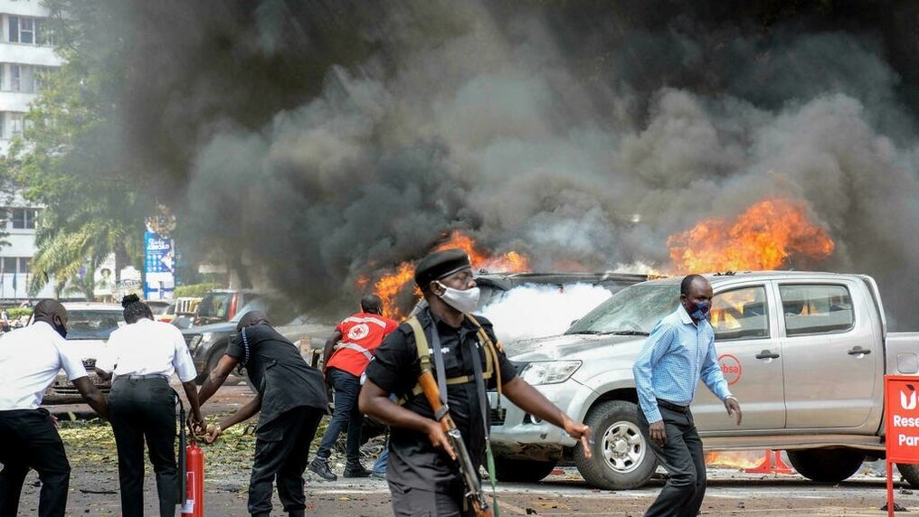Unas personas tratan de apagar las llamas de unos coches incendiados por la explosión de una bomba cerca del Parlamento de Uganda. Foto: AFP.
