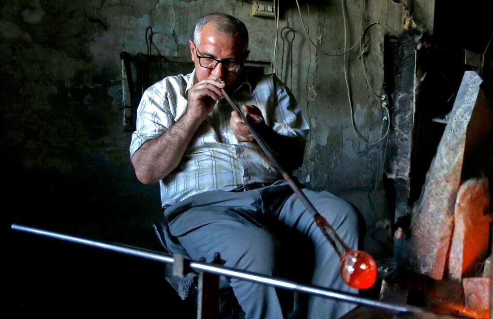 En un taller cerca del centro histórico de Damasco, Mohamed al-Hallak sopla en un largo tubo de metal, inflando el vidrio rojizo. Foto: AFP.