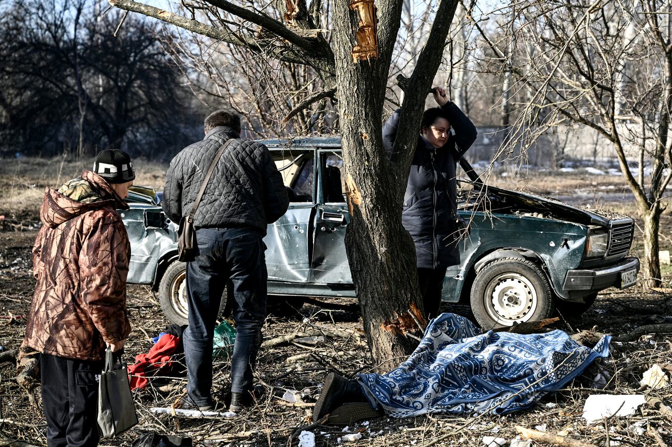 People stand by the body of a relative stretched out on the ground after bombings on the eastern Ukraine town of Chuguiv on February 24, 2022, as Russian armed forces are trying to invade Ukraine from several directions, using rocket systems and helicopters to attack Ukrainian position in the south, the border guard service said. - Russia's ground forces today crossed into Ukraine from several directions, Ukraine's border guard service said, hours after President Vladimir Putin announced the launch of a major offensive. Russian tanks and other heavy equipment crossed the frontier in several northern regions, as well as from the Kremlin-annexed peninsula of Crimea in the south, the agency said. (Photo by Aris Messinis / AFP)